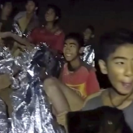In this July 3, 2018, image taken from video provided by the Royal Thai Navy Facebook Page, Thai boy smiles as Thai Navy Seal medic help injured children inside a cave in Mae Sai, northern Thailand. The Thai soccer teammates stranded more than a week in the partly flooded cave said they were healthy on a video released Wednesday, as heavy rains forecast for later this week could complicate plans to safely extract them. (Royal Thai Navy Facebook Page via AP)