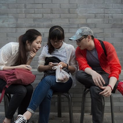 A Chinese woman uses her smartphone as she sits with two friends on a street in Beijing. Photo: AFP