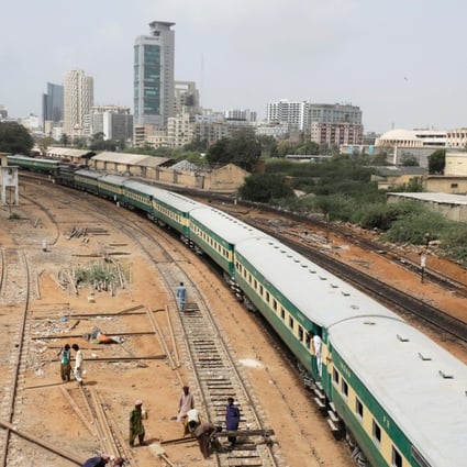 A passenger train passes labourers working on a railway track near City Station in Karachi. Photo: Reuters