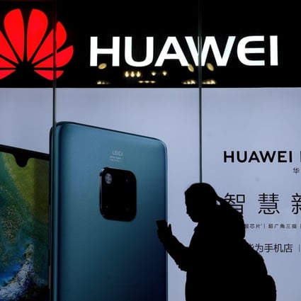 A woman browses her smartphone as she walks by a Huawei store at a shopping mall in Beijing. Photo: AP