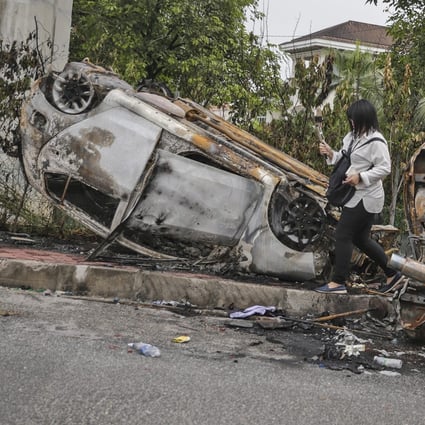 A journalist walks by a burnt car that was flipped upside down during a riot at the Seafields temple. Photo: EP