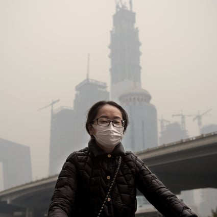 A woman wearing a protective pollution mask cycling in Beijing through thick smog. Photo: AFP