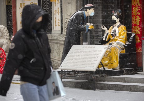 A woman walks past statues wearing face masks, as the snow falls in Beijing on February 5. Photo: AP